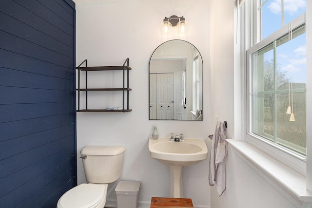 half bathroom featuring toilet, baseboards, and wood walls