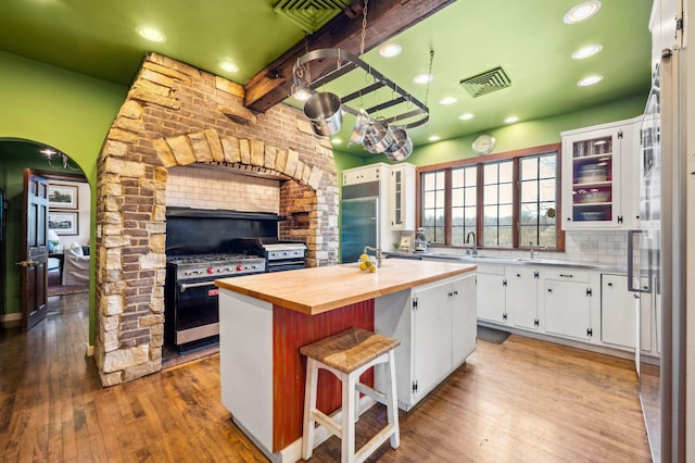 kitchen with hardwood / wood-style floors, visible vents, butcher block counters, a center island, and white cabinetry
