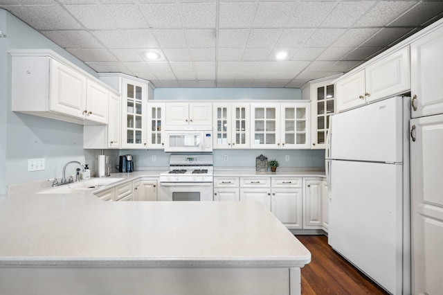 kitchen featuring a peninsula, a sink, dark wood finished floors, white appliances, and light countertops
