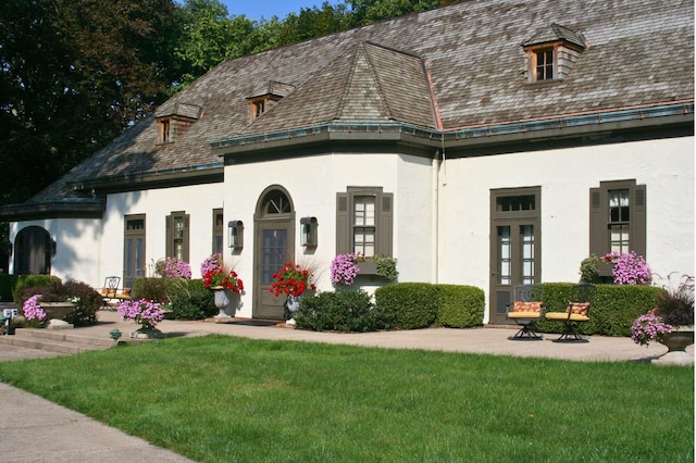 view of front facade with stucco siding, a high end roof, a front yard, and french doors