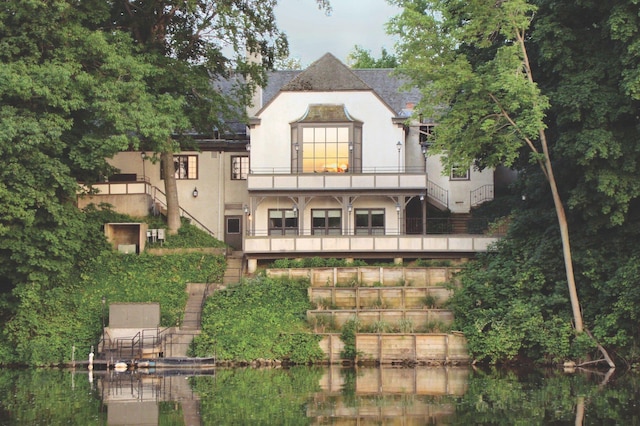 rear view of property with stucco siding, a balcony, a water view, and stairway
