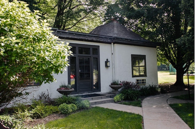 view of front of property featuring roof with shingles, a front yard, and stucco siding