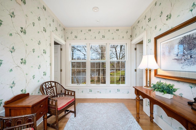 sitting room with wallpapered walls, light wood-style floors, and crown molding