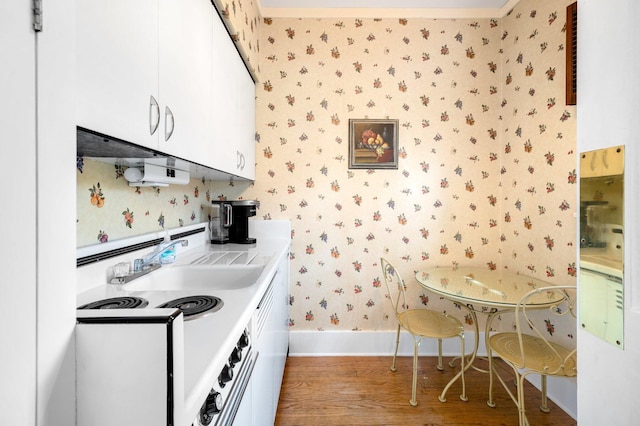 kitchen with white cabinets, wallpapered walls, wood finished floors, and baseboards