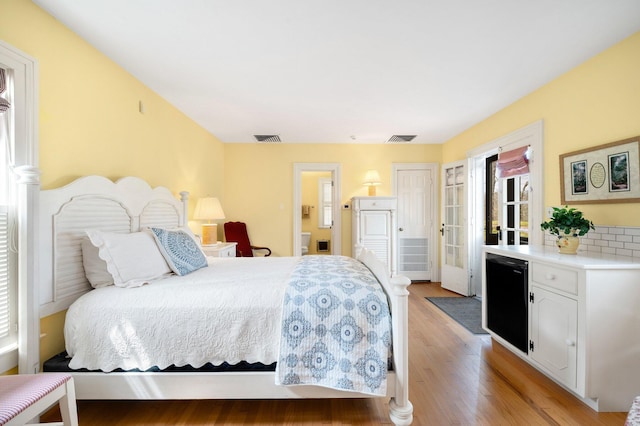 bedroom featuring light wood-style floors, fridge, visible vents, and connected bathroom