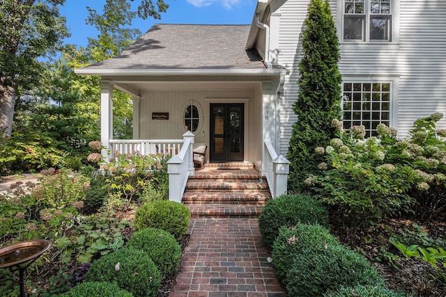 view of exterior entry featuring roof with shingles and a porch