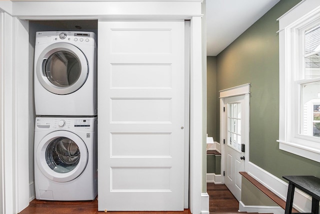 laundry room with laundry area, stacked washer / dryer, dark wood-type flooring, and a healthy amount of sunlight
