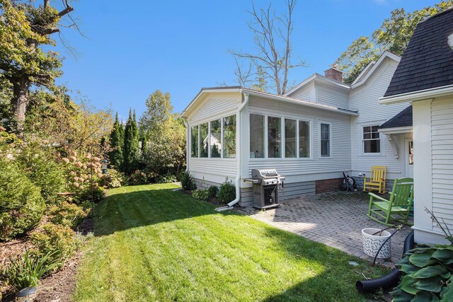 rear view of house with roof with shingles, a chimney, a lawn, a sunroom, and a patio
