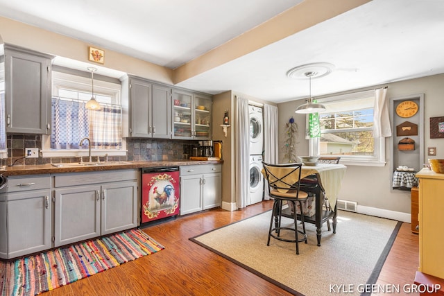 kitchen featuring dishwasher, gray cabinetry, estacked washer and dryer, a sink, and decorative backsplash
