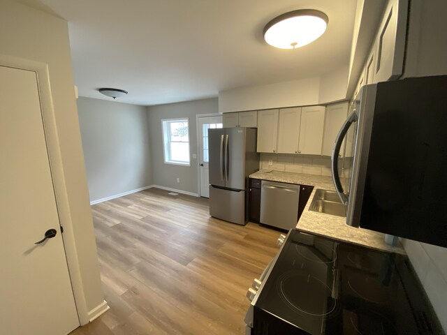 10 Meadow Hills Ln, Fremont, MI 49412 - kitchen featuring light stone countertops, baseboards, light wood-style flooring, tasteful backsplash, and appliances with stainless steel finishes