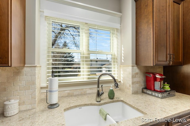 6501 Andres Xing Unit 14, Grandville, MI 49418 - interior details featuring light stone countertops, decorative backsplash, a sink, and brown cabinetry