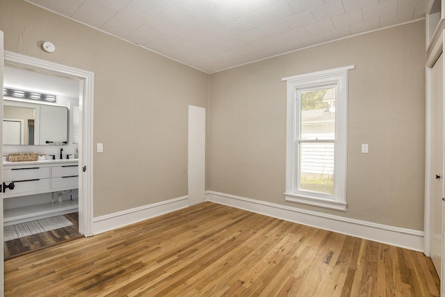 unfurnished bedroom with light wood-style floors, ensuite bath, crown molding, and baseboards