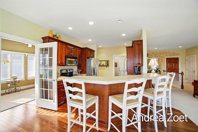 kitchen featuring a kitchen breakfast bar, stainless steel appliances, baseboards, wood finished floors, and a peninsula