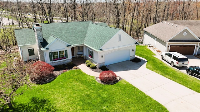 view of front of property with a front yard, stone siding, a chimney, concrete driveway, and an attached garage