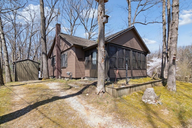view of property exterior featuring a storage shed, an outbuilding, a sunroom, and a chimney