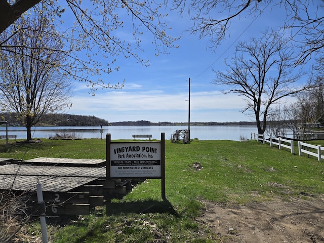 dock area featuring fence, a water view, and a yard