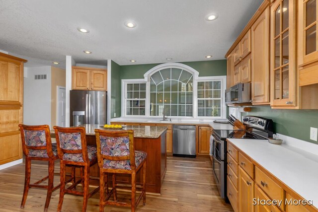 7174 Loma Linda Dr, Rockford, MI 49341 - kitchen featuring stainless steel appliances, a kitchen bar, a kitchen island, wood finished floors, and glass insert cabinets