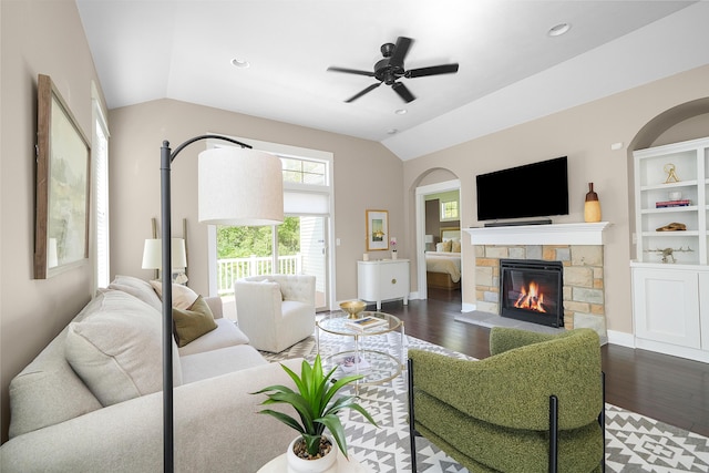 living room featuring a stone fireplace, ceiling fan, wood finished floors, and vaulted ceiling