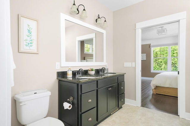 ensuite bathroom with baseboards, a sink, double vanity, and toilet