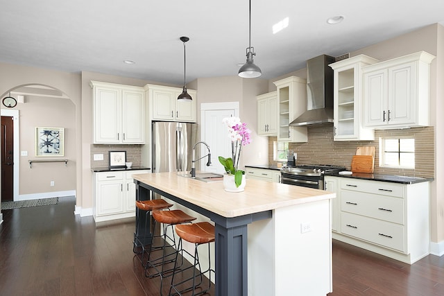 kitchen with appliances with stainless steel finishes, a sink, arched walkways, wall chimney exhaust hood, and baseboards