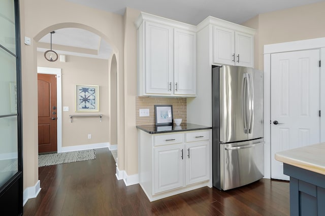 kitchen featuring arched walkways, freestanding refrigerator, white cabinetry, baseboards, and dark wood-type flooring
