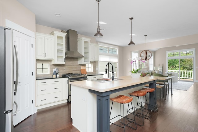 kitchen with dark wood-style flooring, a sink, wall chimney exhaust hood, stainless steel appliances, and a kitchen bar