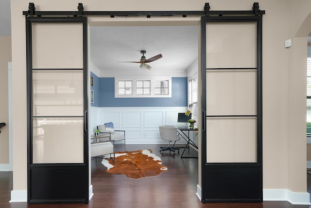 interior space featuring ornamental molding, a barn door, arched walkways, a ceiling fan, and dark wood finished floors
