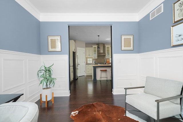sitting room featuring visible vents, ornamental molding, dark wood-style flooring, a decorative wall, and a wainscoted wall