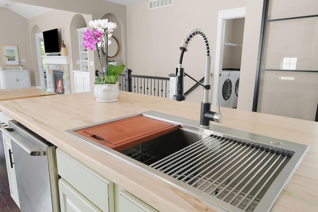kitchen with visible vents, a lit fireplace, washer and clothes dryer, light countertops, and a sink