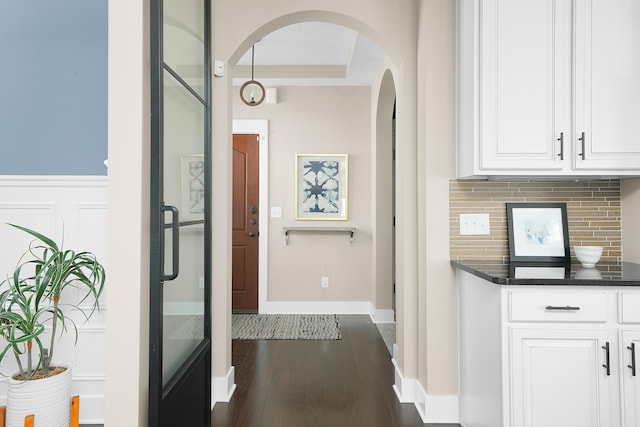 corridor with arched walkways, baseboards, and dark wood finished floors