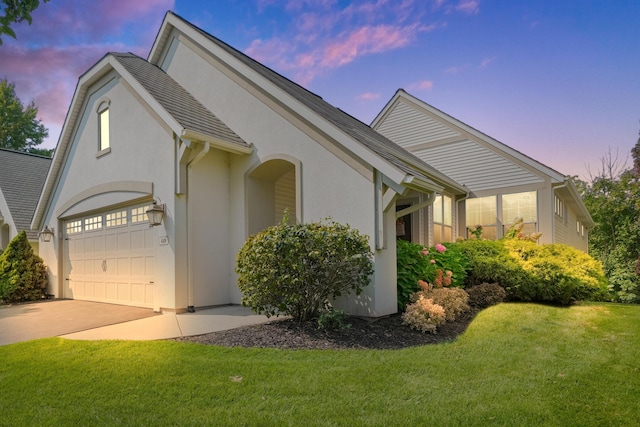 property exterior at dusk with a lawn, concrete driveway, and stucco siding