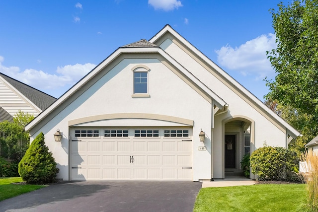 view of front of property featuring an attached garage, aphalt driveway, a front lawn, and stucco siding