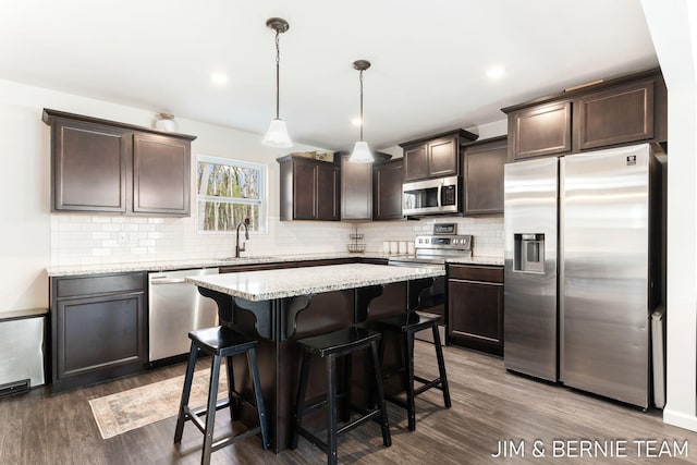 kitchen with a sink, dark wood-style flooring, dark brown cabinetry, a kitchen bar, and appliances with stainless steel finishes