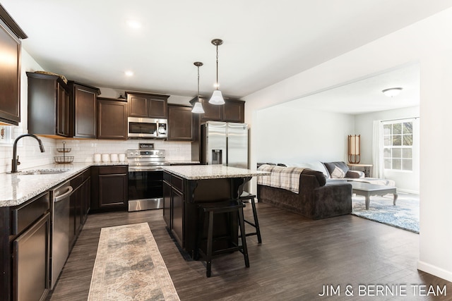 kitchen featuring stainless steel appliances, a sink, a kitchen island, dark brown cabinetry, and tasteful backsplash