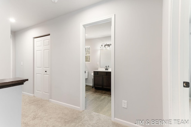 hallway featuring carpet, baseboards, and a sink