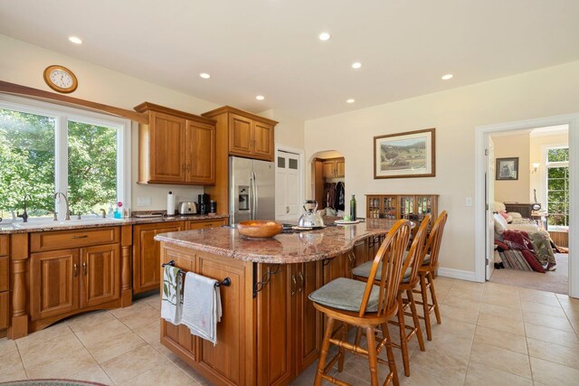 1280 Sylvan Rd, Chelsea, MI 48118 - kitchen with light tile patterned flooring, brown cabinetry, stainless steel refrigerator with ice dispenser, and light stone counters