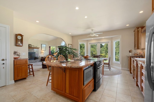 1280 Sylvan Rd, Chelsea, MI 48118 - kitchen with a tiled fireplace, recessed lighting, a ceiling fan, brown cabinets, and a breakfast bar area