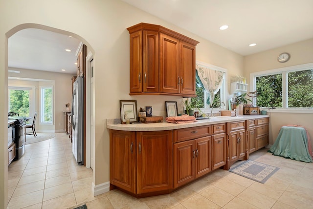 1280 Sylvan Rd, Chelsea, MI 48118 - kitchen with brown cabinets, light tile patterned floors, arched walkways, light countertops, and freestanding refrigerator