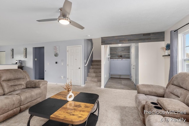 living area featuring light colored carpet, baseboards, a ceiling fan, and stairway