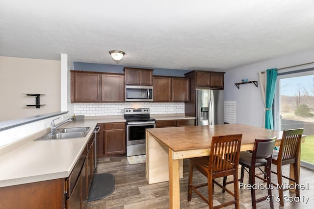 kitchen featuring tasteful backsplash, wood finished floors, a sink, light countertops, and appliances with stainless steel finishes