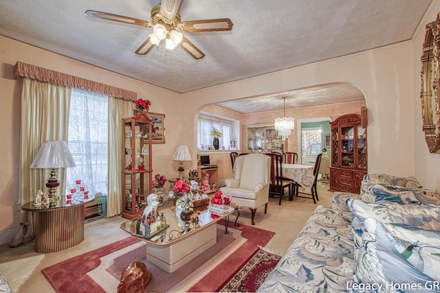 carpeted living room featuring arched walkways, a textured ceiling, plenty of natural light, and ceiling fan with notable chandelier