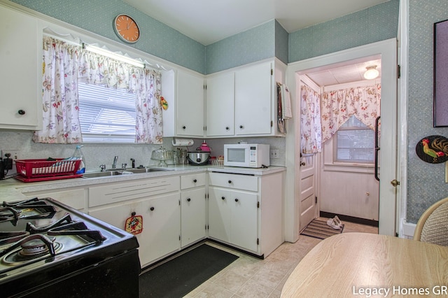 kitchen featuring a sink, white microwave, gas stove, and wallpapered walls