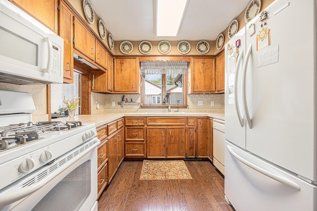 kitchen featuring brown cabinetry, white appliances, a sink, dark wood-type flooring, and light countertops