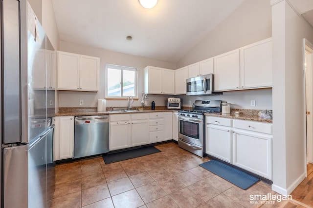 kitchen with white cabinetry, a sink, stone counters, vaulted ceiling, and stainless steel appliances