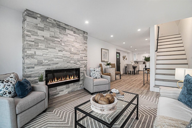 living area with a fireplace, light wood-style floors, recessed lighting, and stairs