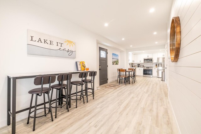 interior space with recessed lighting, light wood-type flooring, baseboards, a dry bar, and appliances with stainless steel finishes