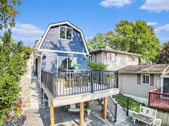 back of property featuring a gambrel roof, a wooden deck, and stairway
