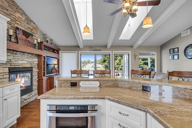 kitchen with a ceiling fan, visible vents, dark wood finished floors, and vaulted ceiling with skylight