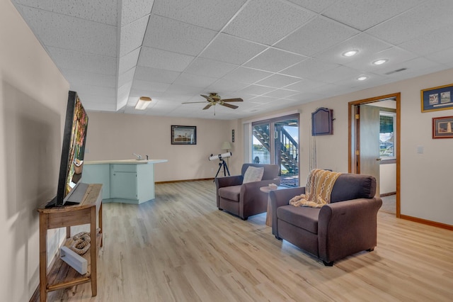 living room with baseboards, a drop ceiling, and ceiling fan