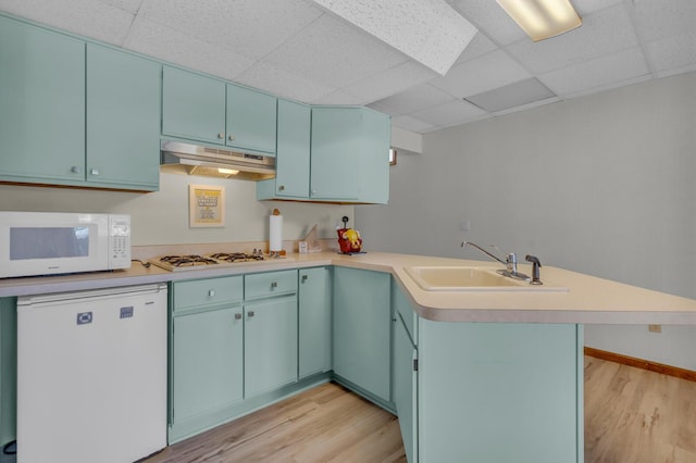 kitchen featuring a sink, a peninsula, light wood finished floors, under cabinet range hood, and white appliances
